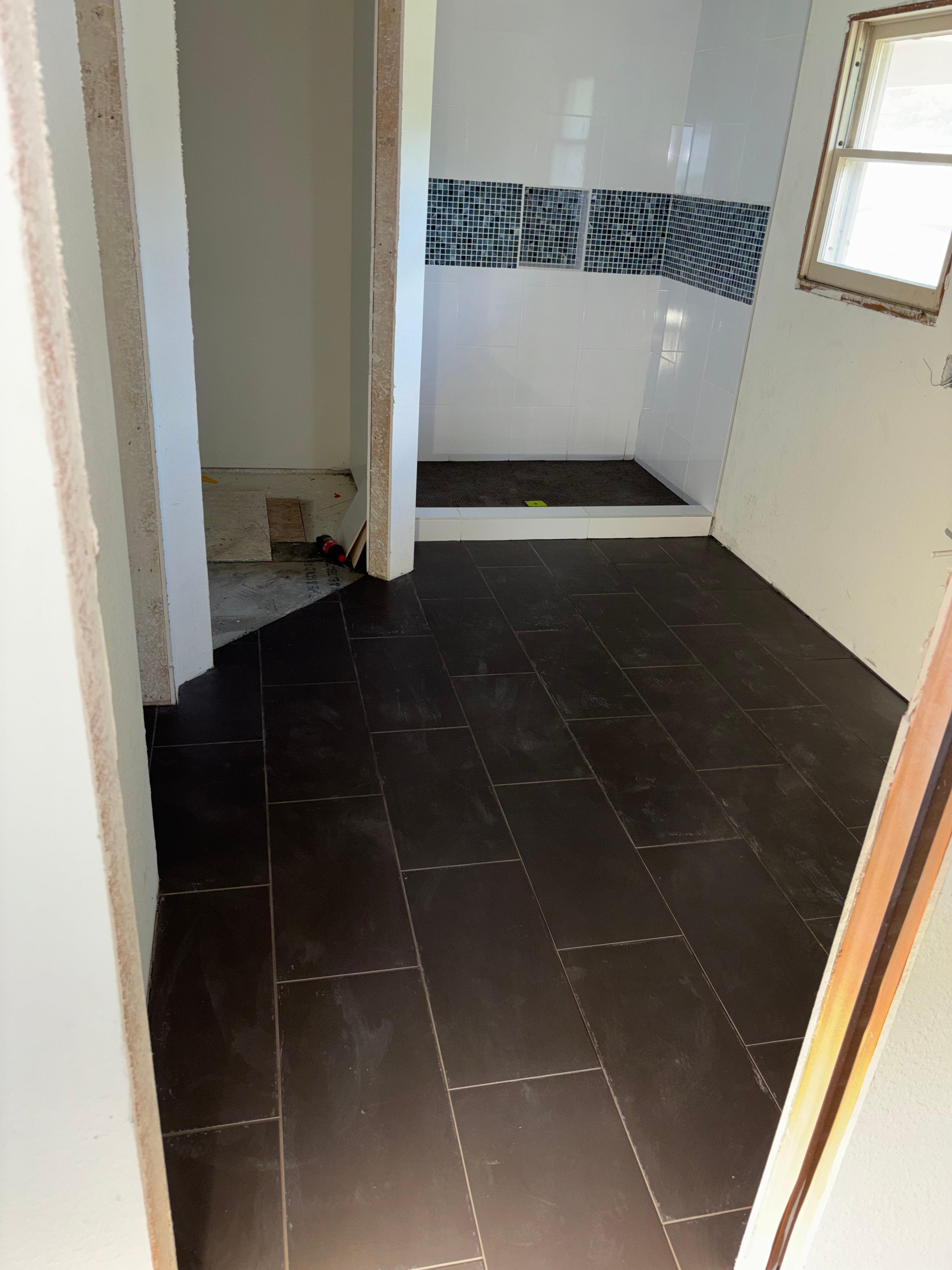 Dark tile shower wall and mosaic accent strip installed during a Gutierrez Flooring bathroom remodel