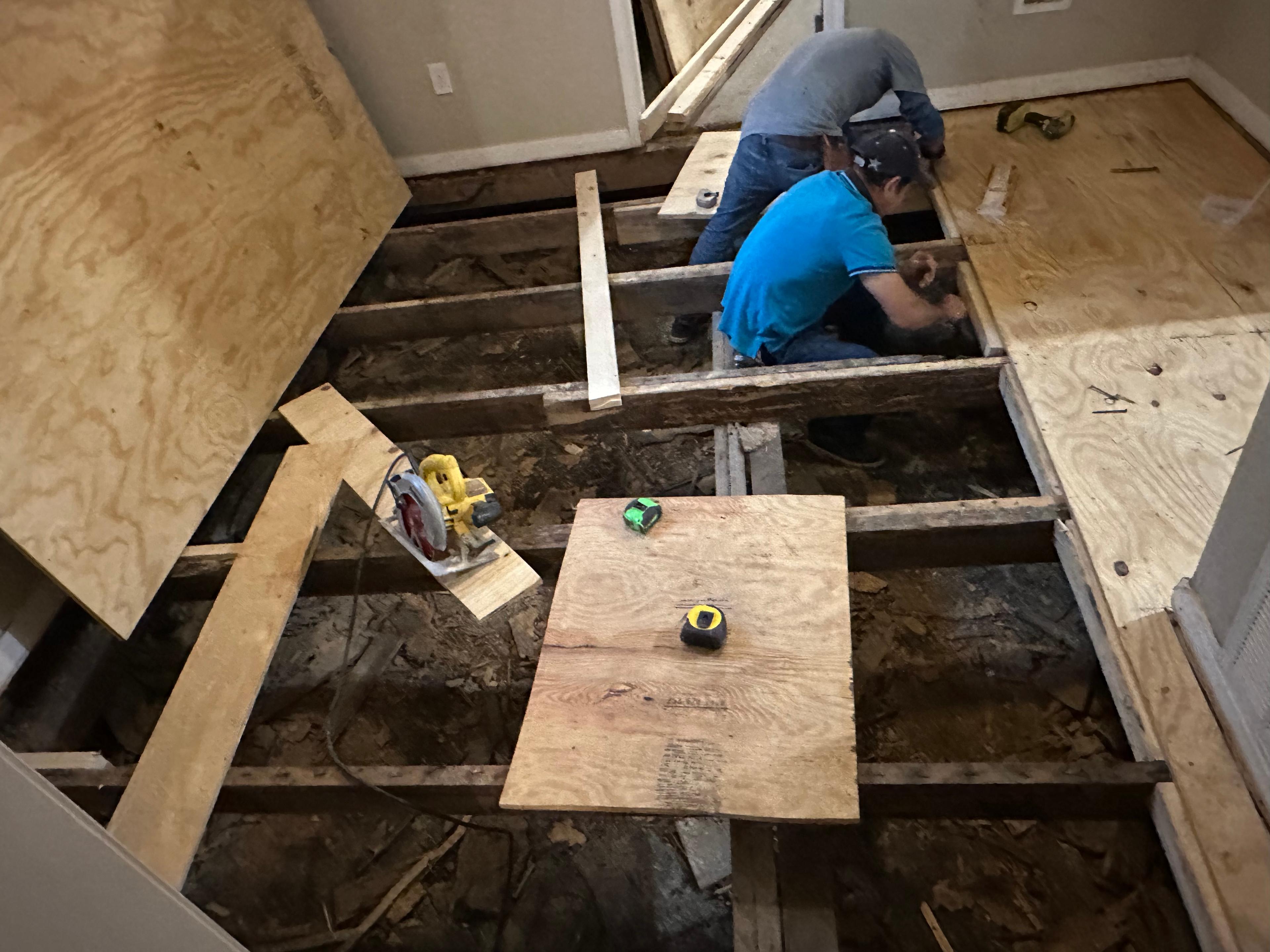 Installers repairing floor joists and patching subfloor plywood beneath a home