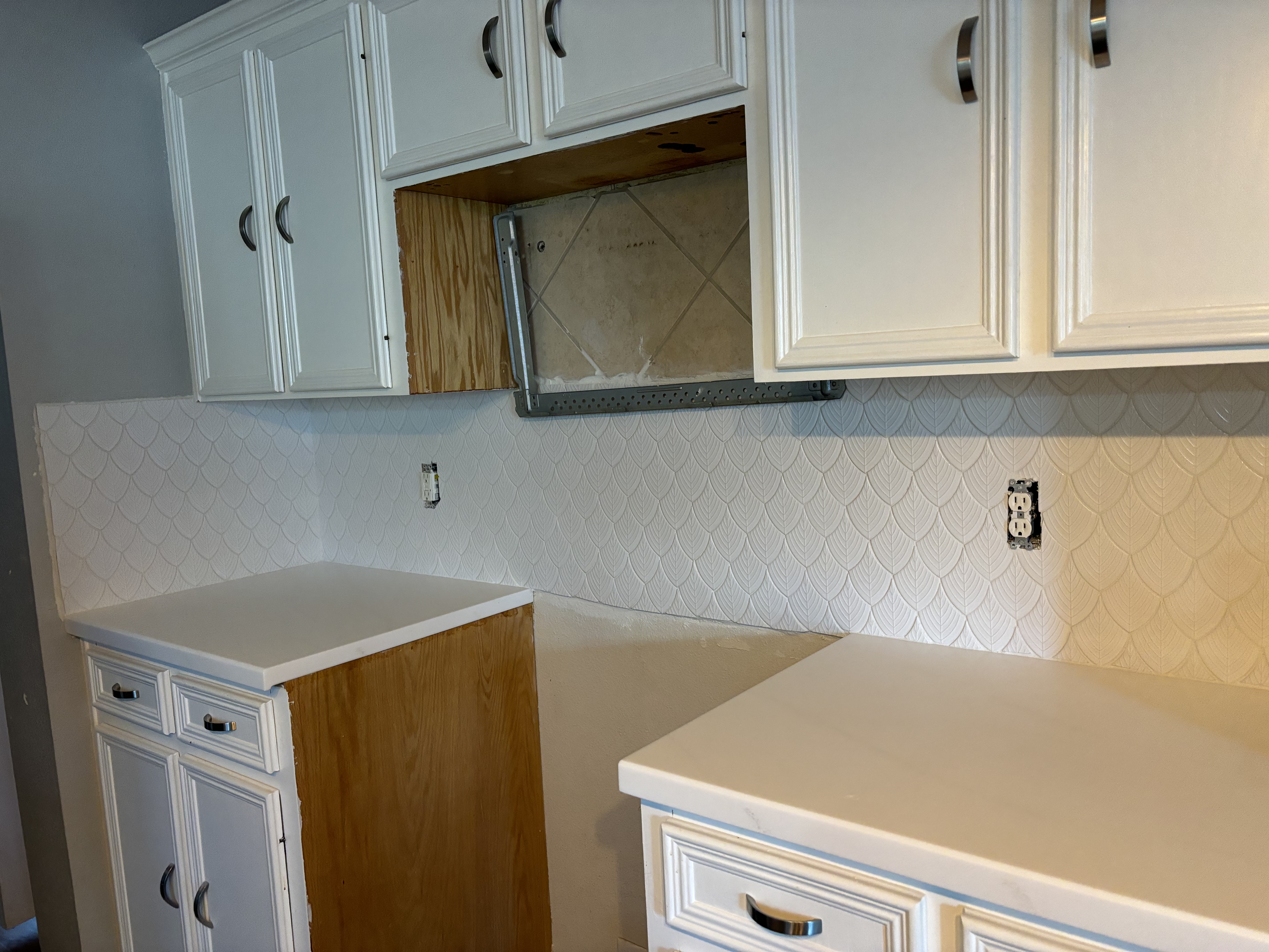 New scalloped tile backsplash installed between white kitchen cabinets, with one upper cabinet still open.