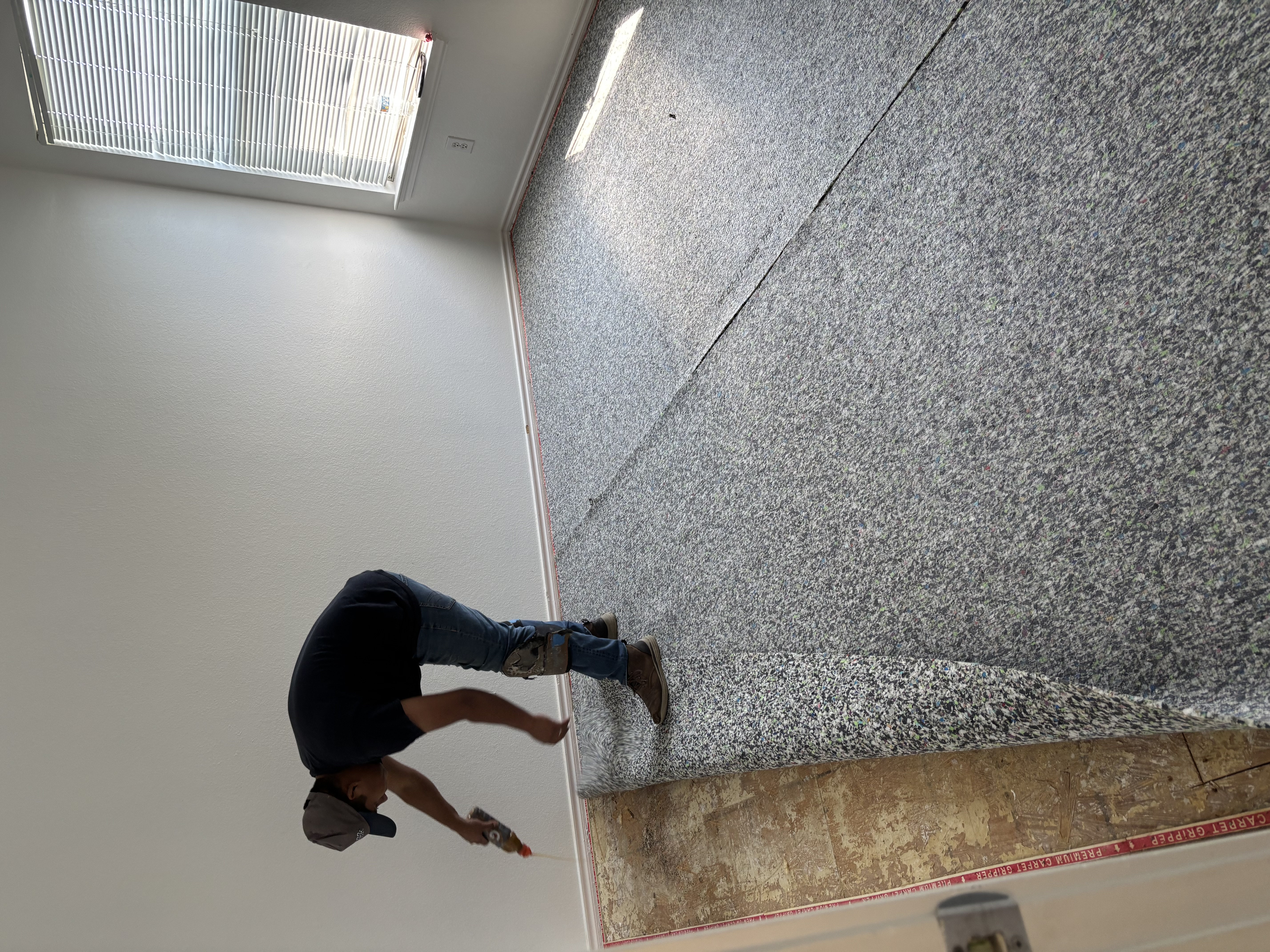 A Gutierrez Flooring installer rolling out new carpet during an installation.