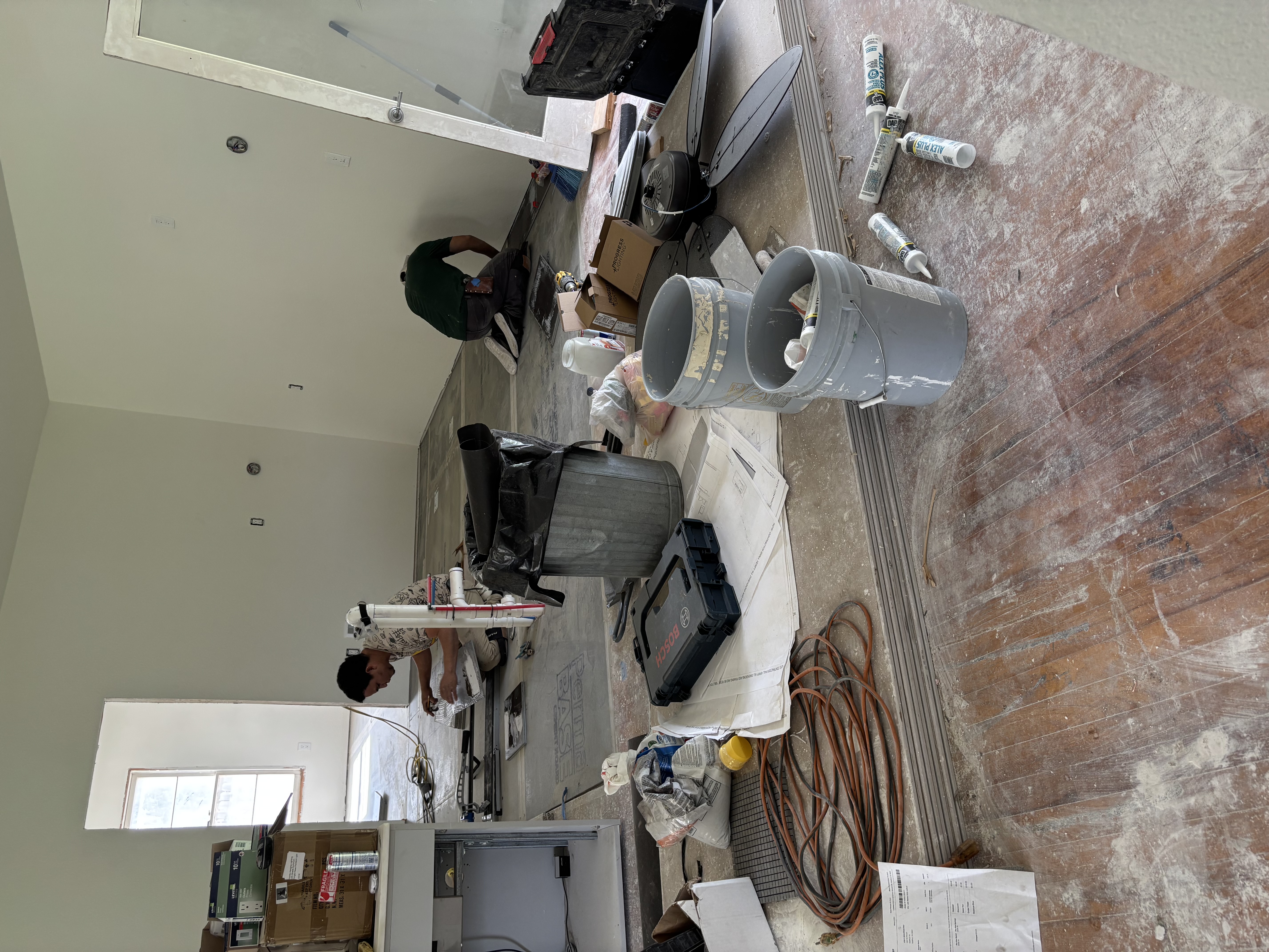 Adhesive buckets, caulk and tools staged on a job site floor before a Gutierrez Flooring installation begins.