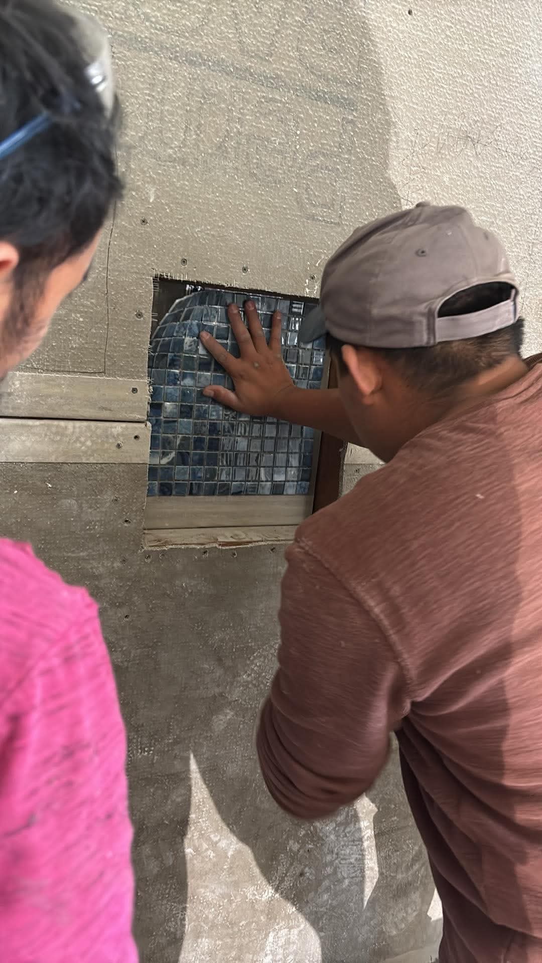 Two Gutierrez Flooring crew members working together to finish a mosaic tile shower niche.