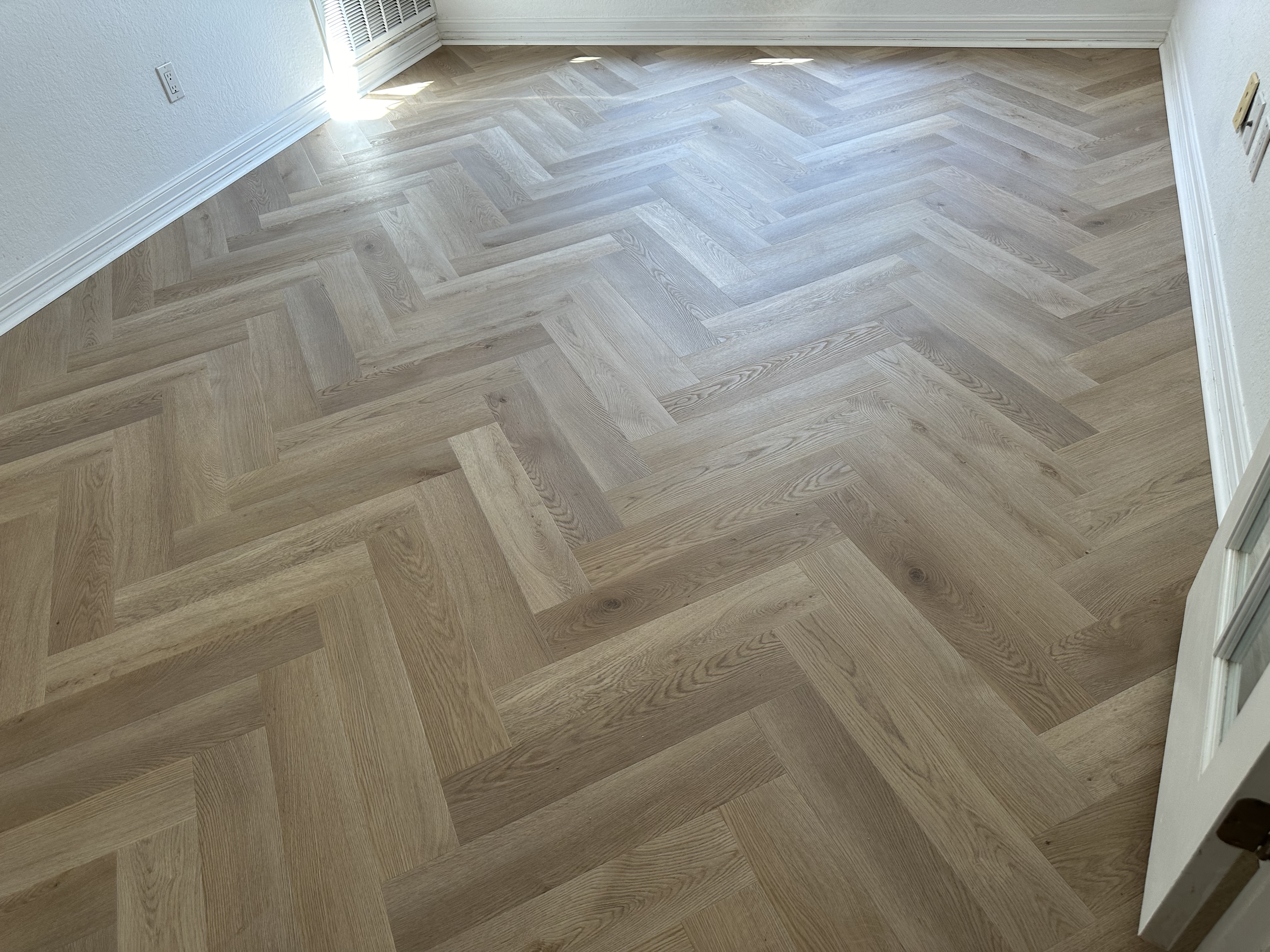 Wood-look luxury vinyl plank laid in a herringbone pattern across a bright, freshly finished room