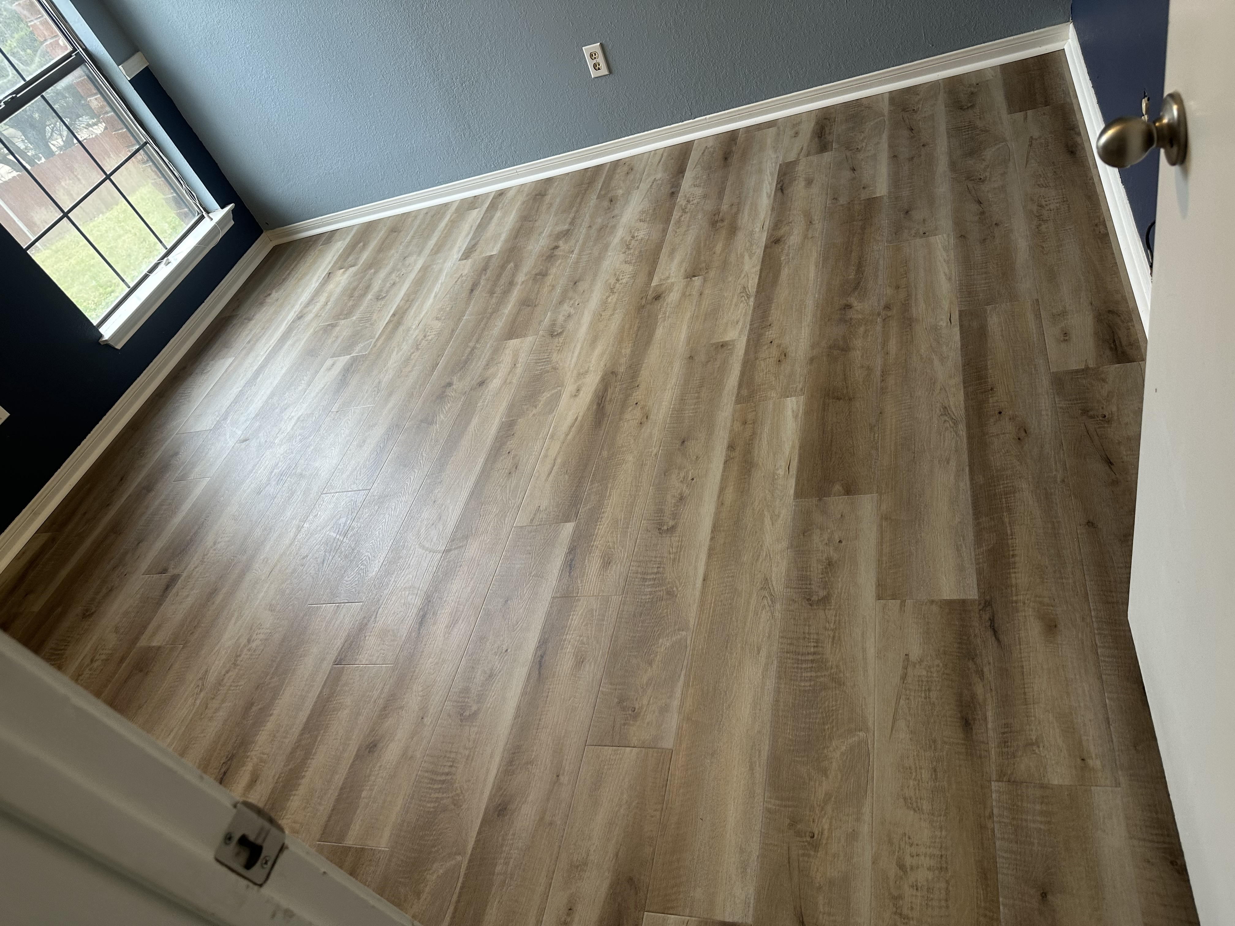 Light oak luxury vinyl plank flooring finished in a freshly painted bedroom with deep navy walls