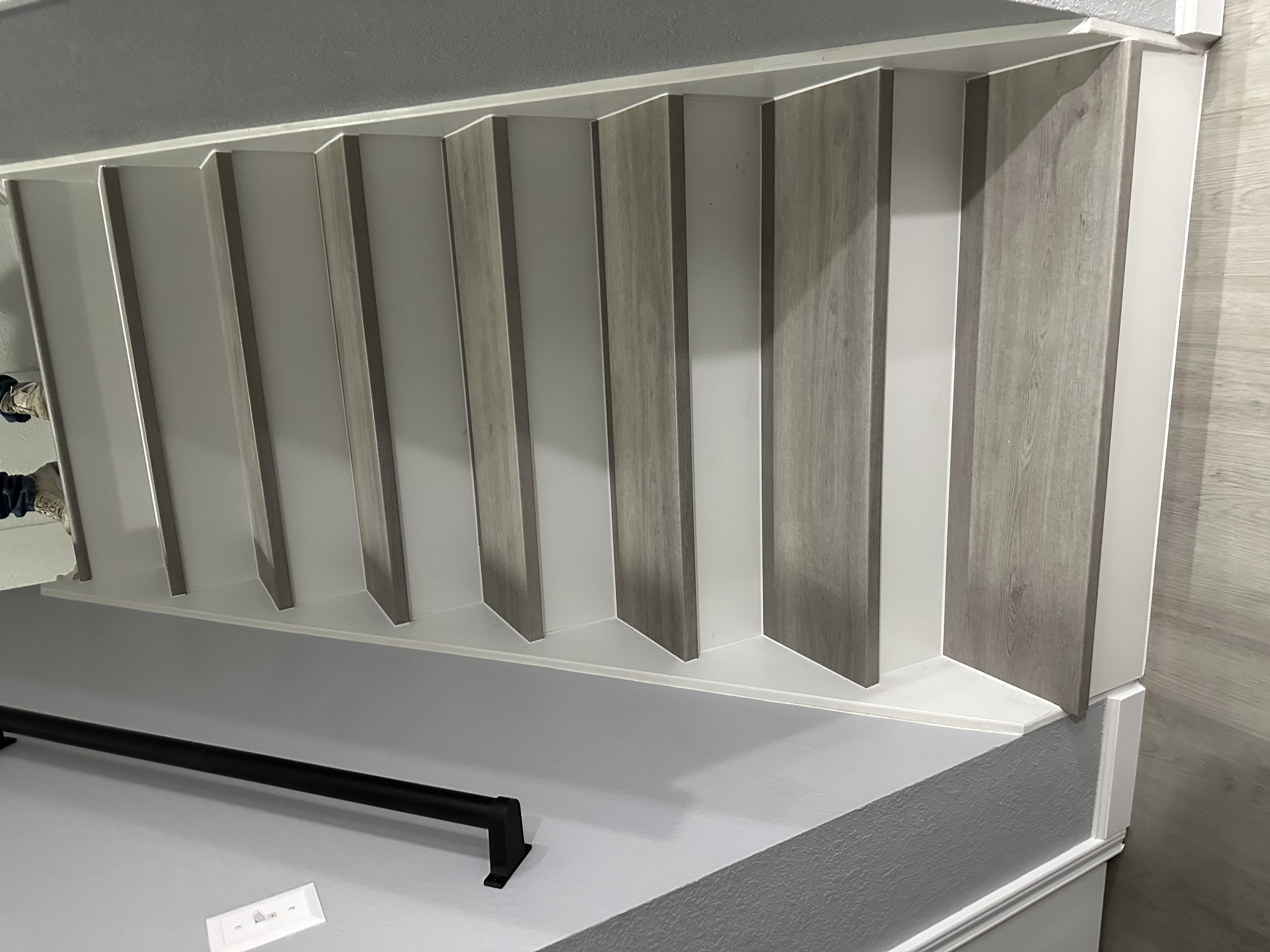 Staircase clad in gray wood-look vinyl plank treads with crisp white risers and a black metal handrail