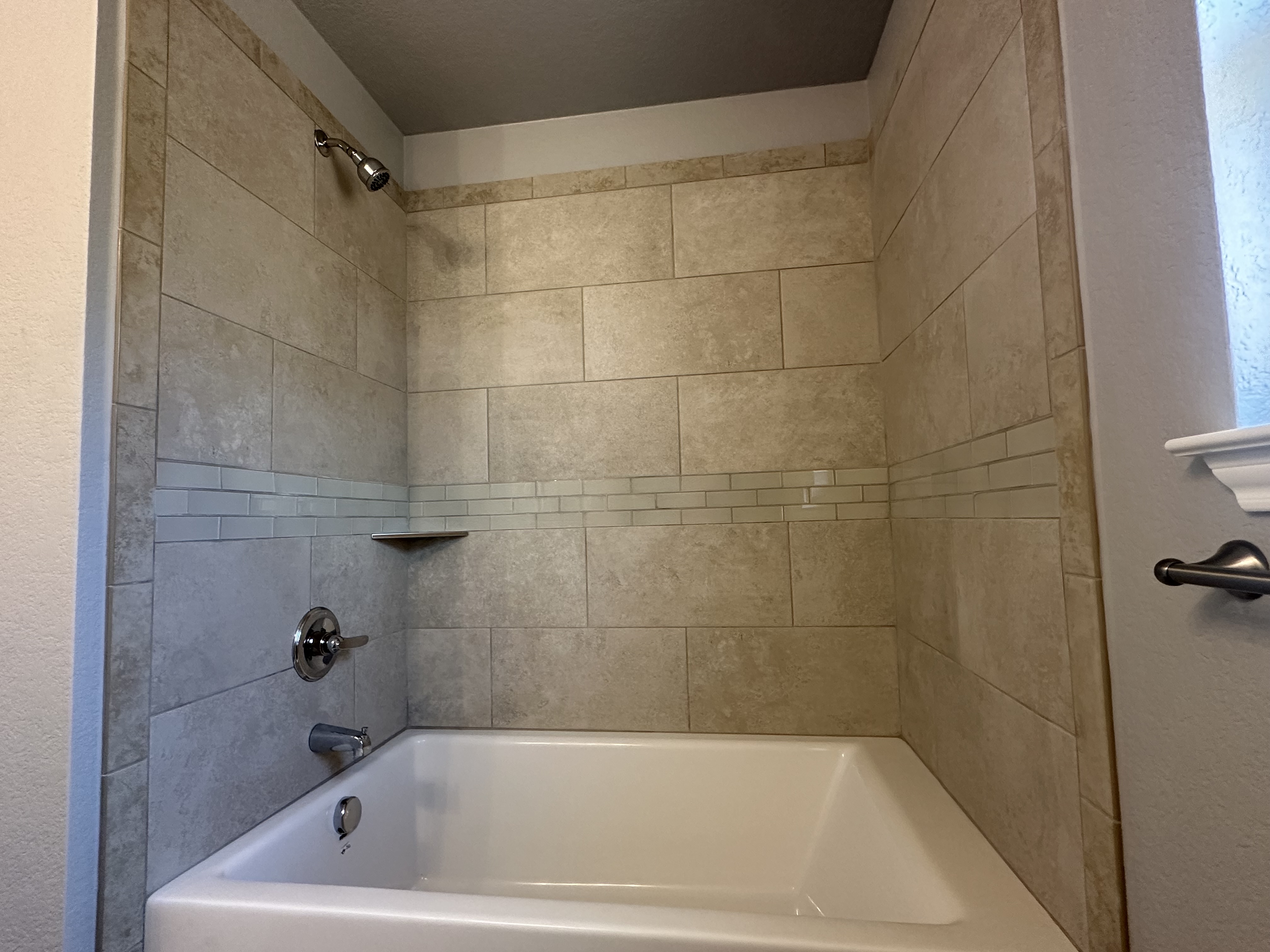 Bathtub and shower surround tiled in beige stone-look tile with a glass mosaic accent band